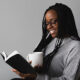 Une jeune femme souriante, une tasse à la main, lit un livre.