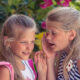 Une petite fille blonde parle à l’oreille de son amie.